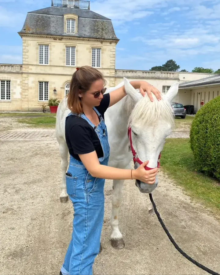 Léa Laplace, une main sur le chanfrein d’un cheval gris, l’autre sur son licol, dans la cour d’une propriété
